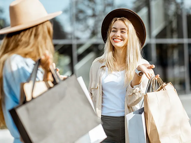 Joyful women shopping together, stylish hats complementing their trendy outfits, carrying chic shopping bags in a vibrant urban setting.