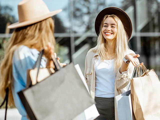 Joyful shopping experience with two fashionable women smiling and carrying shopping bags outdoors.