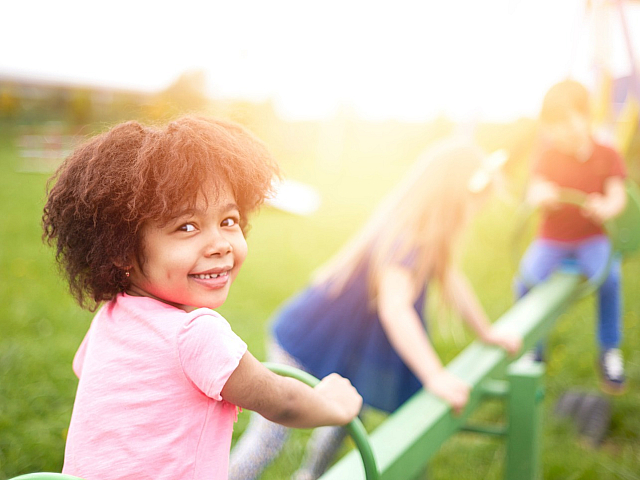 Joyful child playing on a seesaw in a sunny, green park setting.