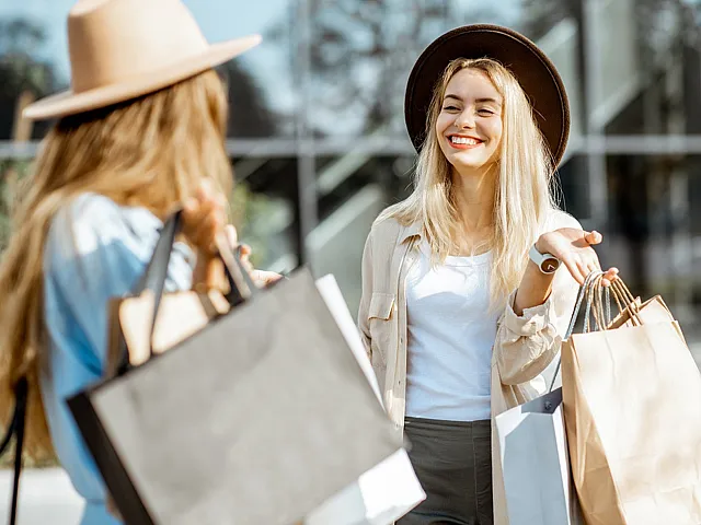Joyful shopping experience with two stylish women holding shopping bags, smiling brightly under sunny skies.