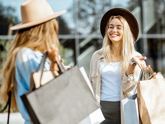 Two stylish women enjoying a cheerful shopping day with a modern glass building in the background.