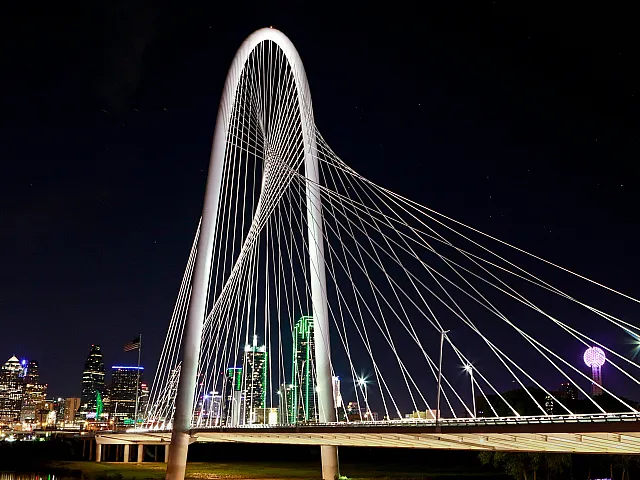Stunning nighttime view of a modern cable-stayed bridge illuminated against a vibrant cityscape, showcasing architectural elegance and urban charm.
