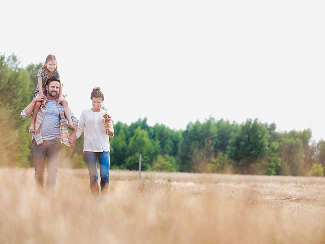 Happy family enjoying a walk through a sunlit field surrounded by lush greenery, capturing the essence of nature and togetherness.