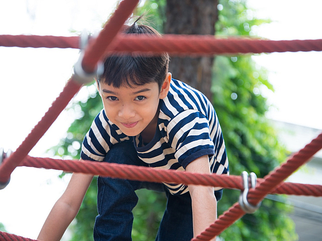 Joyful child playing on a red rope climbing structure in a vibrant outdoor park setting.