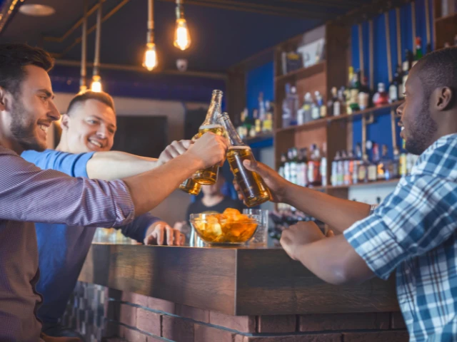 Friends enjoying drinks together at a lively bar with bottled beverages, warm hanging lights, and a modern lounge atmosphere.