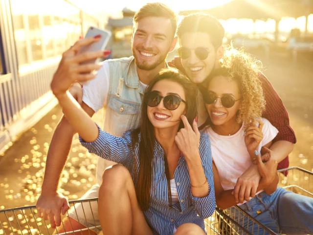 Group of friends taking a selfie together outdoors at sunset while sitting in a shopping cart, smiling and enjoying a fun, carefree moment.
