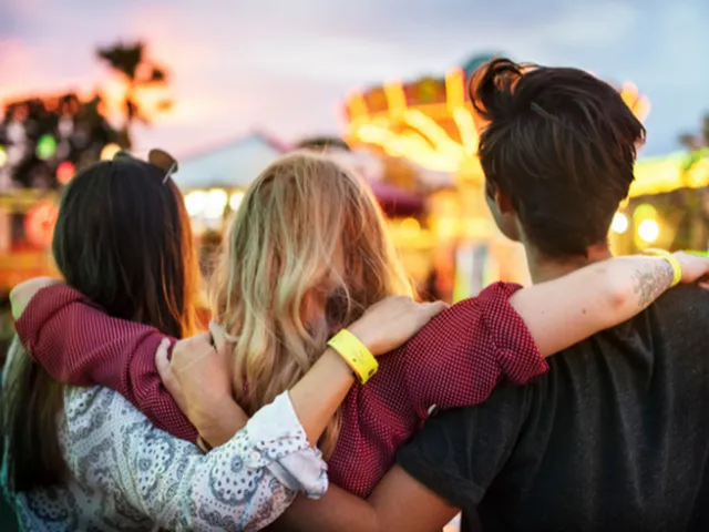 Three friends embracing and enjoying a lively fair at sunset, creating joyful memories together with colorful lights in the background.