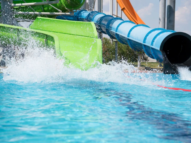Colorful water slides splash into a sparkling swimming pool at a nearby water park. Bright green and blue enclosed slides create an exciting setting for outdoor recreation, family fun, and warm-weather entertainment.