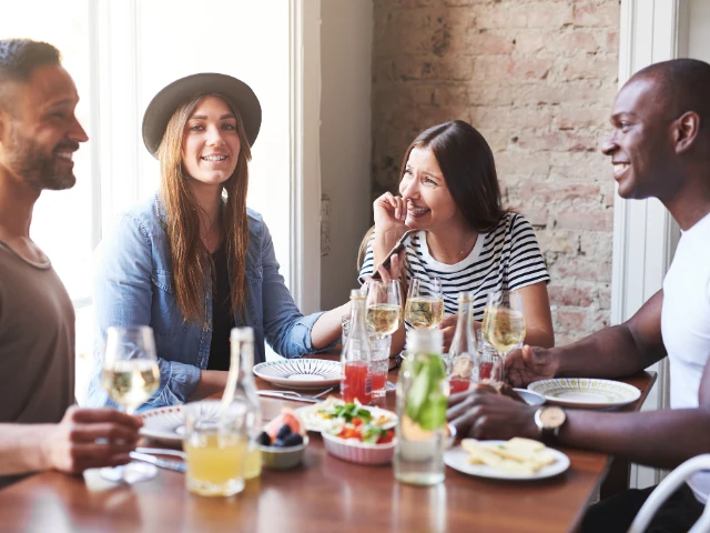 Group of friends enjoying a meal together around a dining table, smiling and socializing in a bright, welcoming setting.