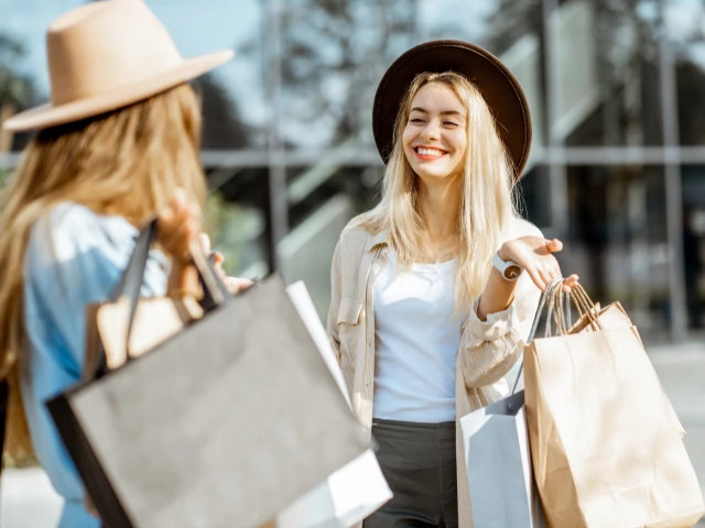 Two friends enjoying a day of shopping outdoors, smiling and chatting while carrying shopping bags.