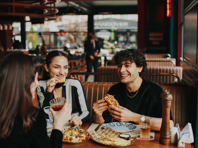 Friends enjoying a meal together at a lively restaurant, sharing food and conversation around a table.