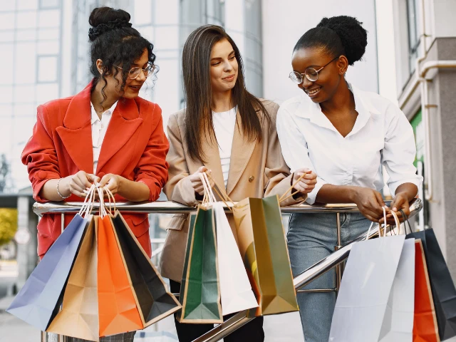 Three friends enjoying a shopping trip together while carrying colorful shopping bags outdoors.