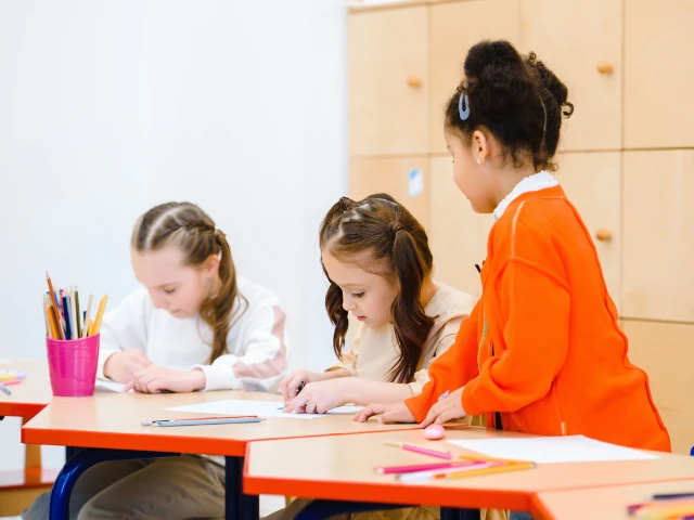 Young students drawing and working together at a classroom table with colorful pencils and art supplies.