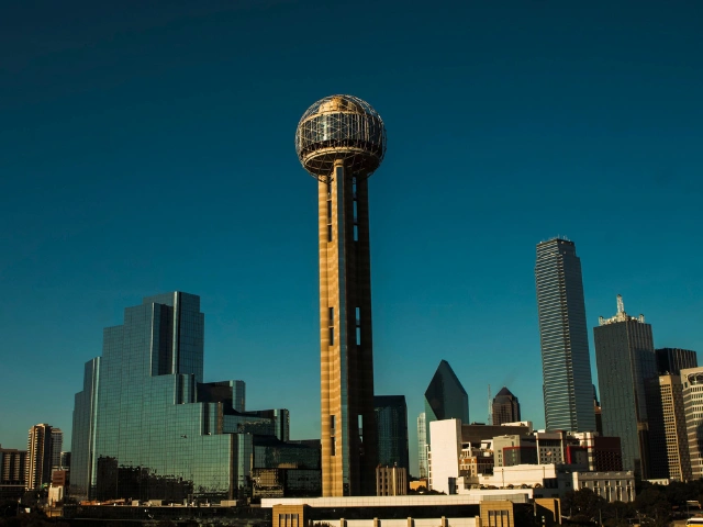 Reunion Tower and the Downtown Dallas skyline under a clear blue sky.