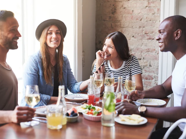 Group of four friends smiling and enjoying food and drinks together at a restaurant table.
