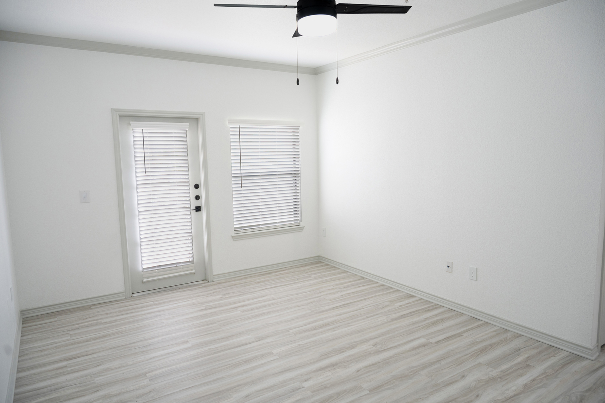 Bright modern room with sleek laminate flooring, a large window, and a ceiling fan, perfect for stylish living.
