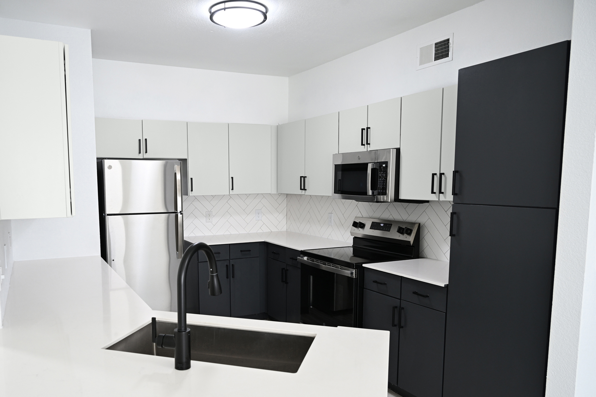 Sleek modern kitchen with stainless steel appliances, chic white countertops, and elegant herringbone backsplash.