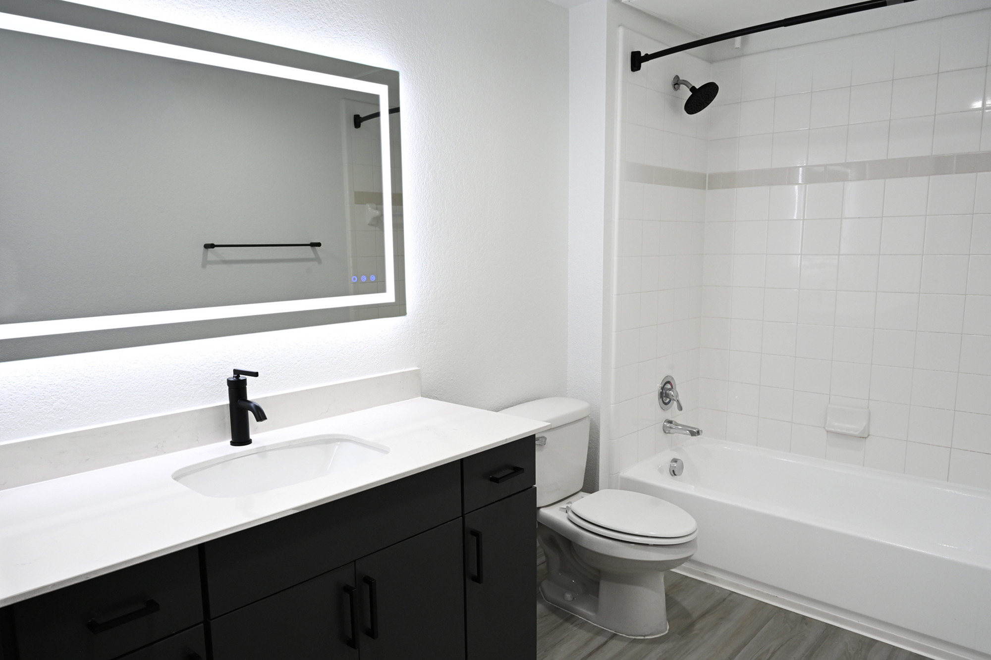 Elegant modern bathroom featuring a sleek black vanity, illuminated mirror, and pristine white bathtub.