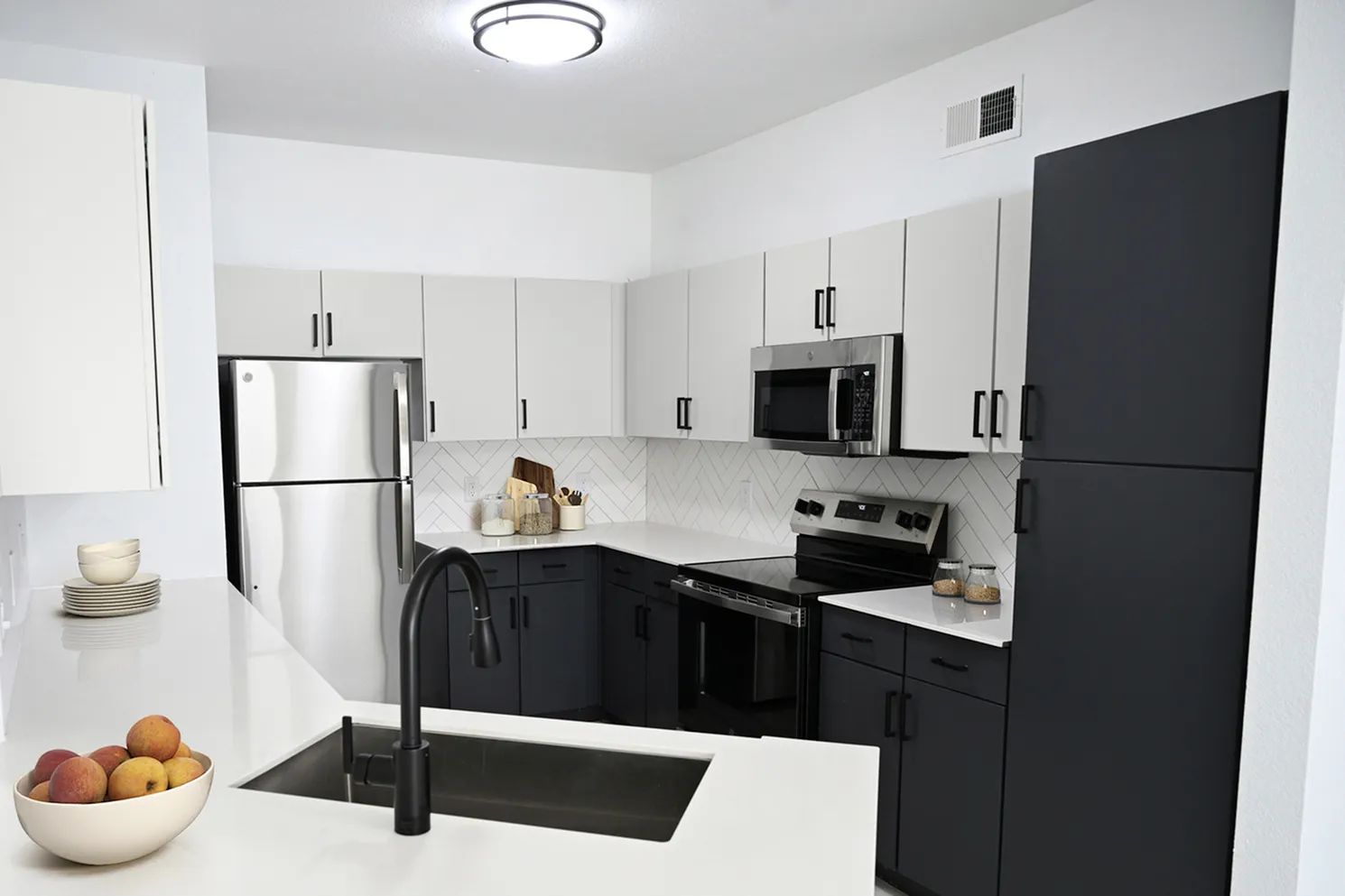 Modern kitchen with sleek black and white cabinetry, stainless steel appliances, and a stylish chevron tile backsplash.