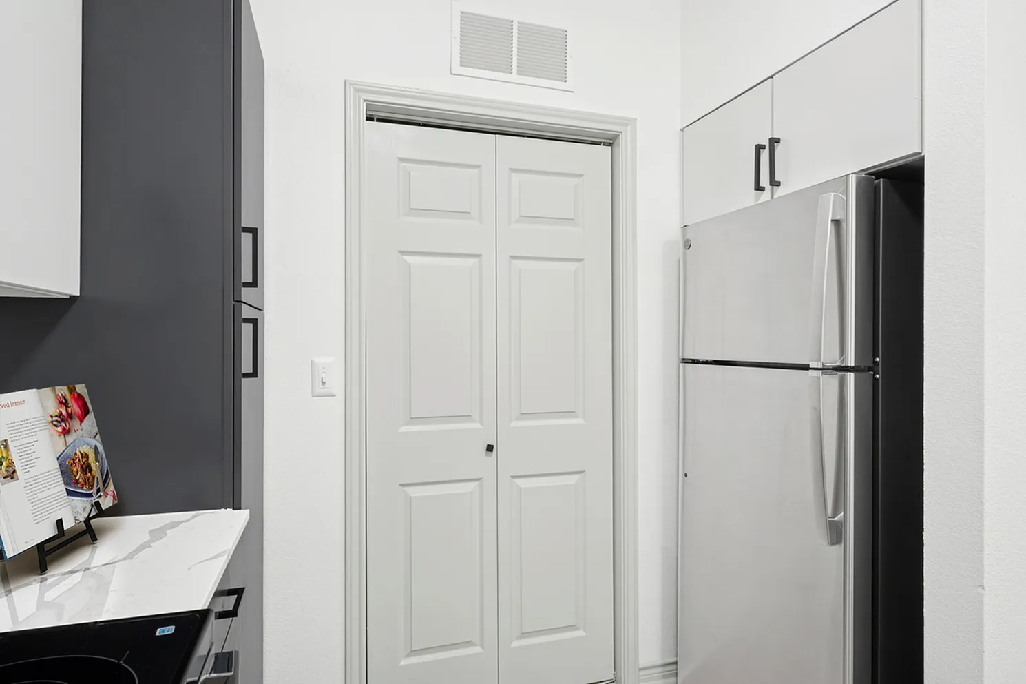 Modern kitchen corner featuring a sleek stainless steel refrigerator, stylish cabinetry, and elegant marble countertop.