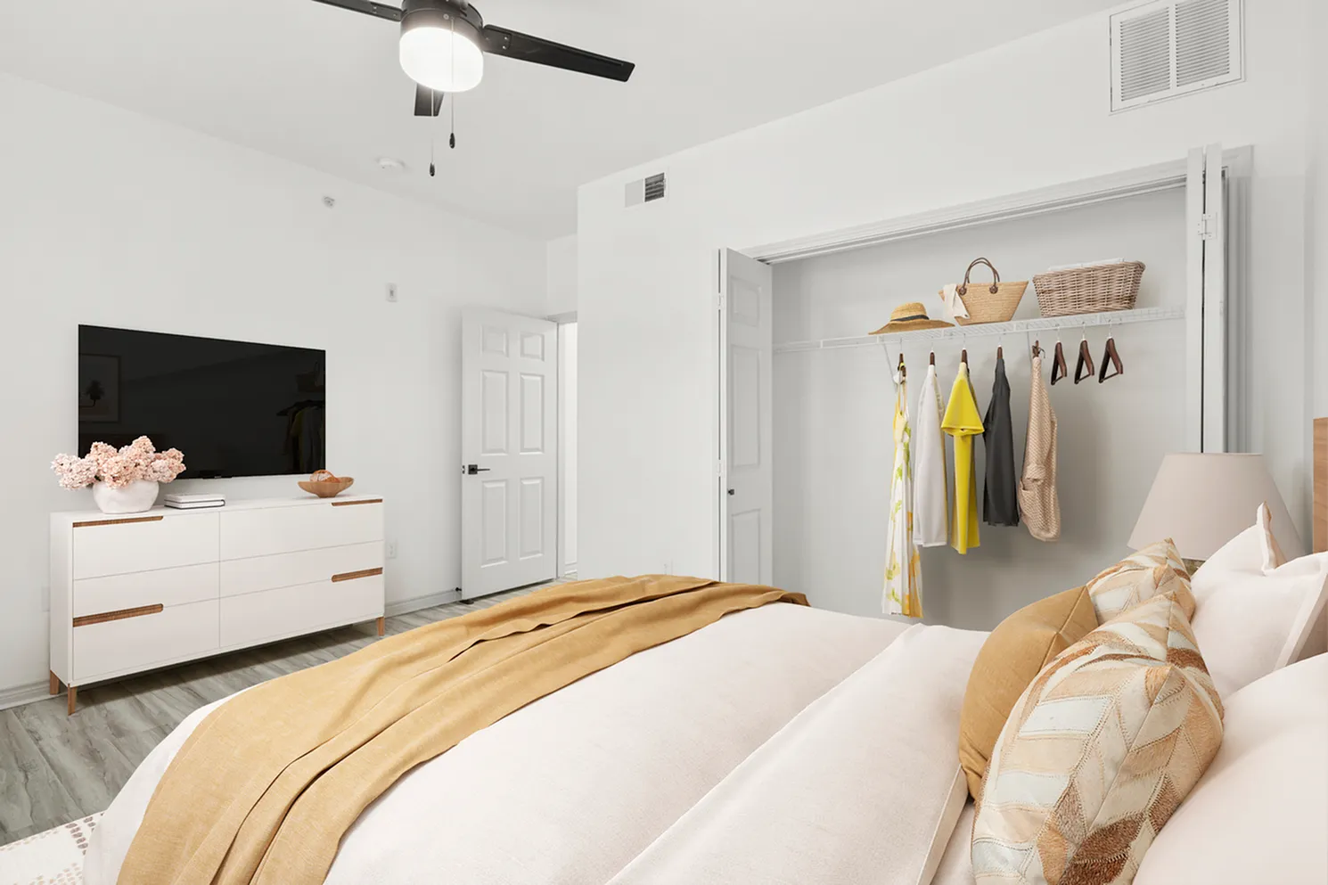 Bright and inviting bedroom with stylish decor, featuring a cozy bed, elegant dresser with a TV, and a spacious open closet with organized clothing and accessories.
