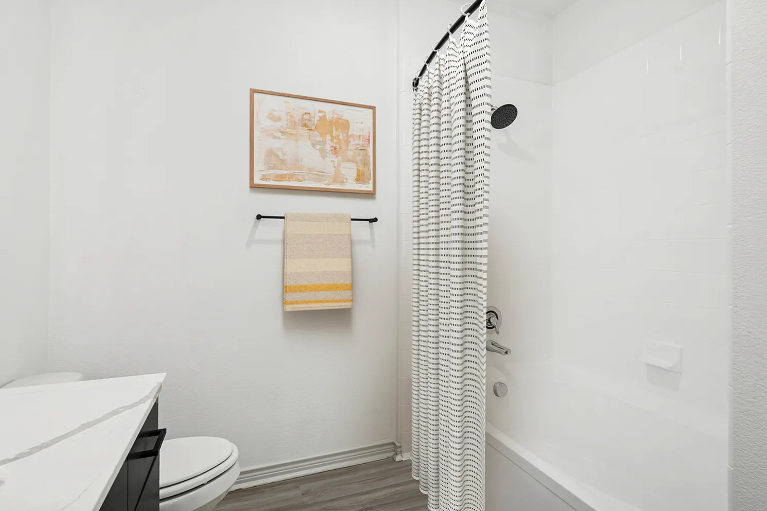Bright and modern bathroom featuring a sleek white bathtub, elegant striped shower curtain, and contemporary artwork, creating a refreshing and stylish atmosphere.