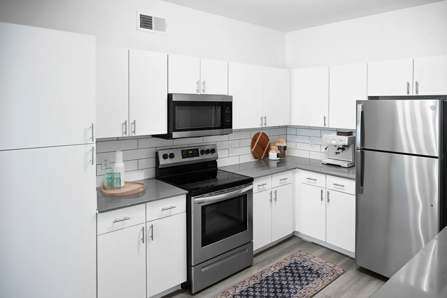 Modern kitchen with sleek white cabinets, stainless steel appliances, and elegant black countertops, featuring a cozy vibe with a stylish blue rug.