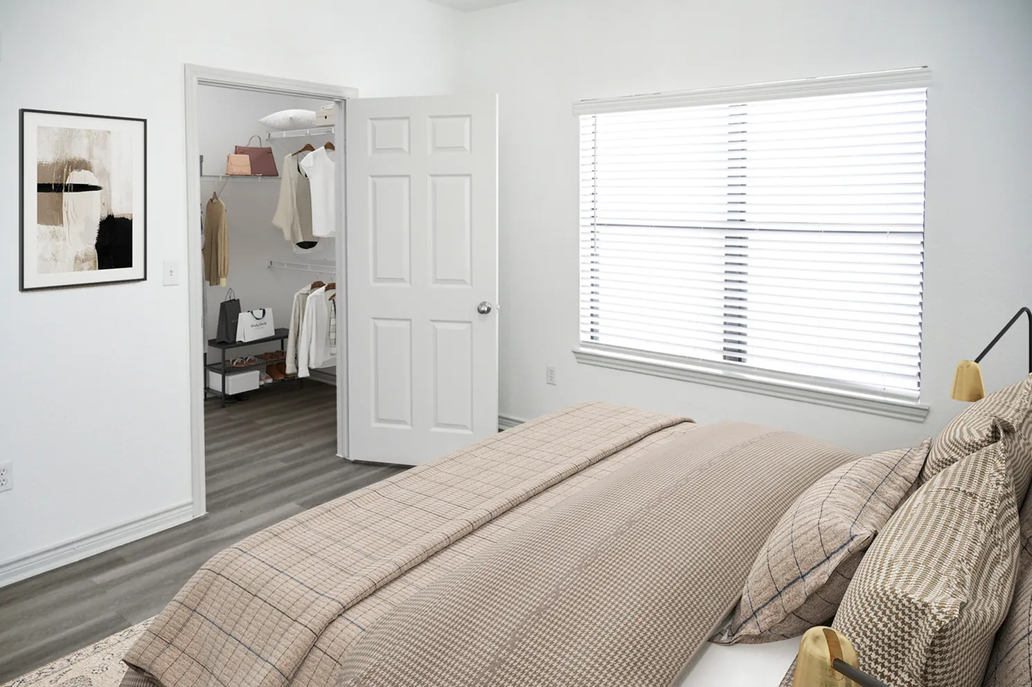 Bright bedroom with cozy bedding, an open walk-in closet, large window, and elegant artwork on the wall.