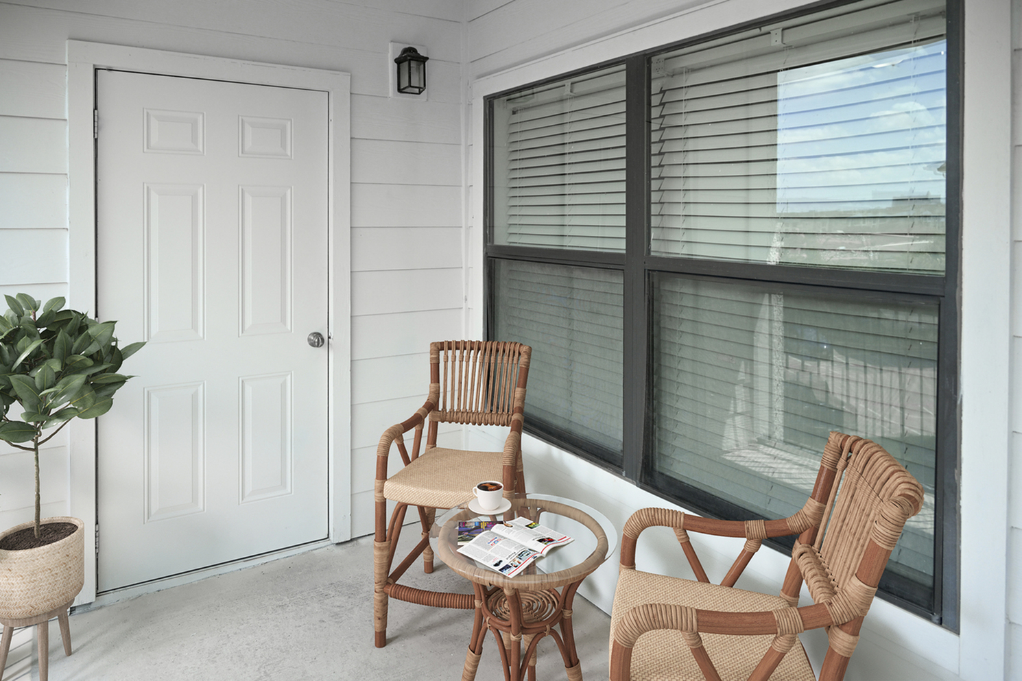 Inviting patio with cozy wicker chairs, a small glass table, and lush potted plant, perfect for relaxation.