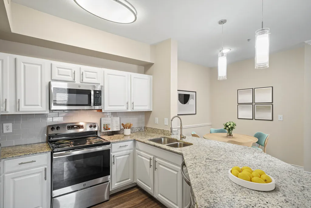 Modern kitchen with sleek white cabinets, stainless steel appliances, and a granite countertop featuring a breakfast bar. Contemporary dining area with elegant pendant lighting creating a cozy ambiance.