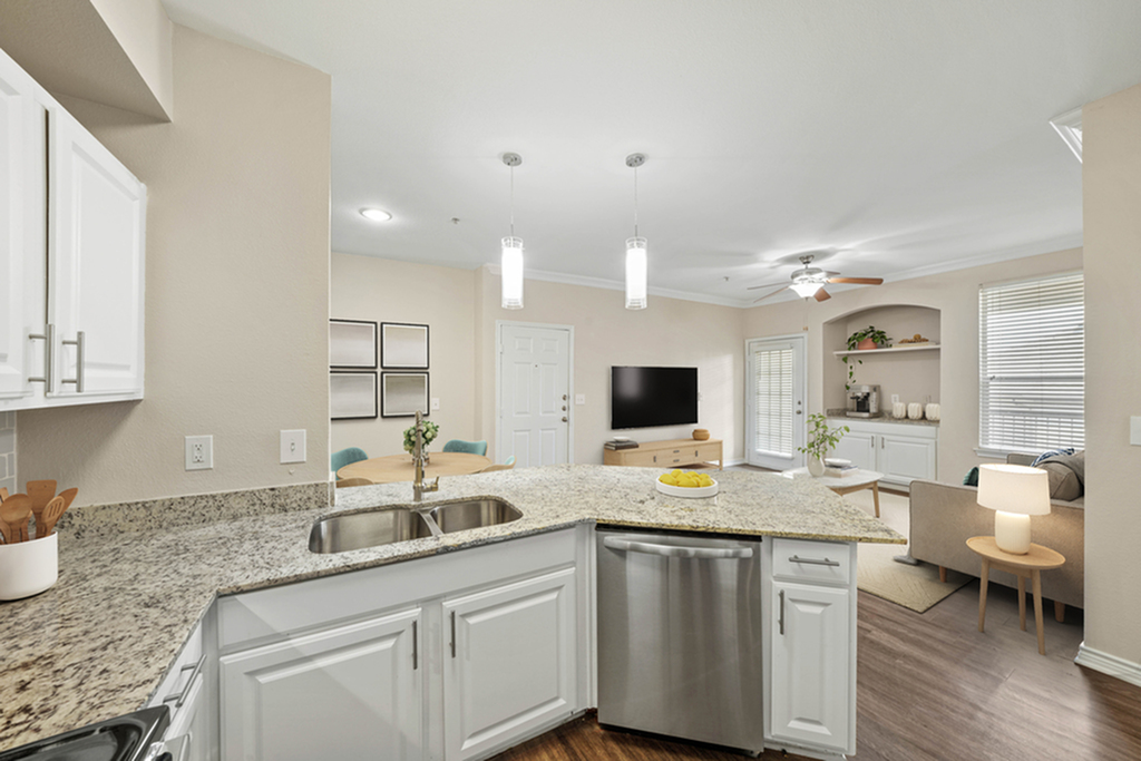 Modern open-plan kitchen and living room with elegant granite countertops, stylish pendant lighting, and a cozy seating area.