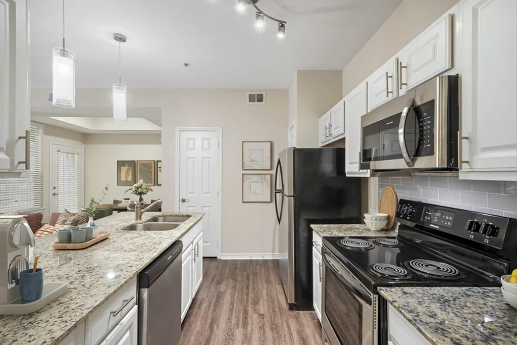 Open concept kitchen with granite counters, pendant lighting, wood floors, stainless appliances, white cabinets, and wooden floors