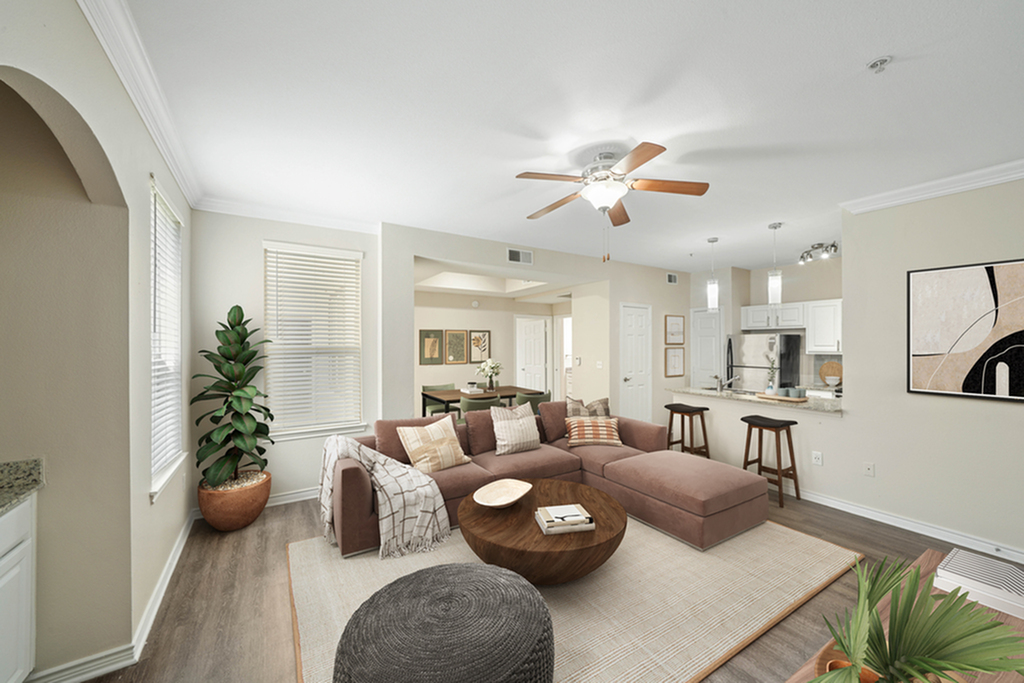 Living room with hardwood floor, large brown sectional, ceiling fan, round coffee table, and large plotted plant