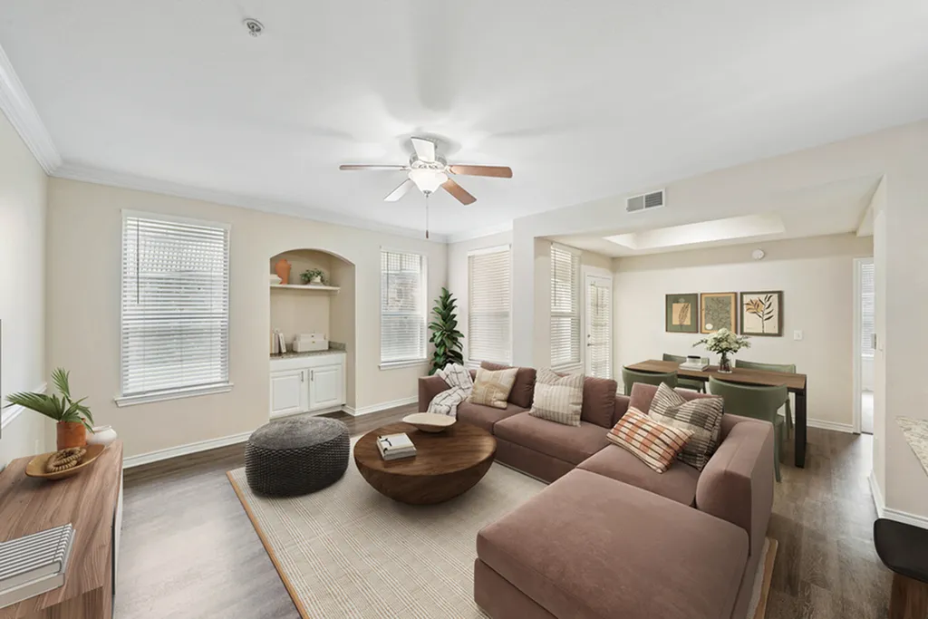 Living room with hardwood floor, window, large brown sectional, ceiling fan, round coffee table, and large plotted plant