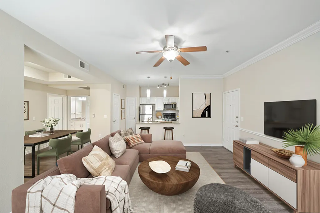 Living room with hardwood floor, large brown sectional, ceiling fan, round coffee table, and large plotted plant, overlooking dining area with dining table and chairs