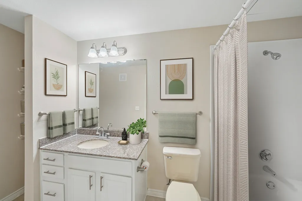 Bathroom with granite counters, vanity lighting and large mirror, toilet, wall art, and towel racks with green towels