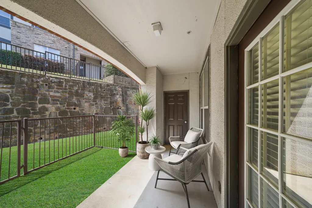 Patio with lush green grass, black railing, patio chairs with pillow, and potted plants.