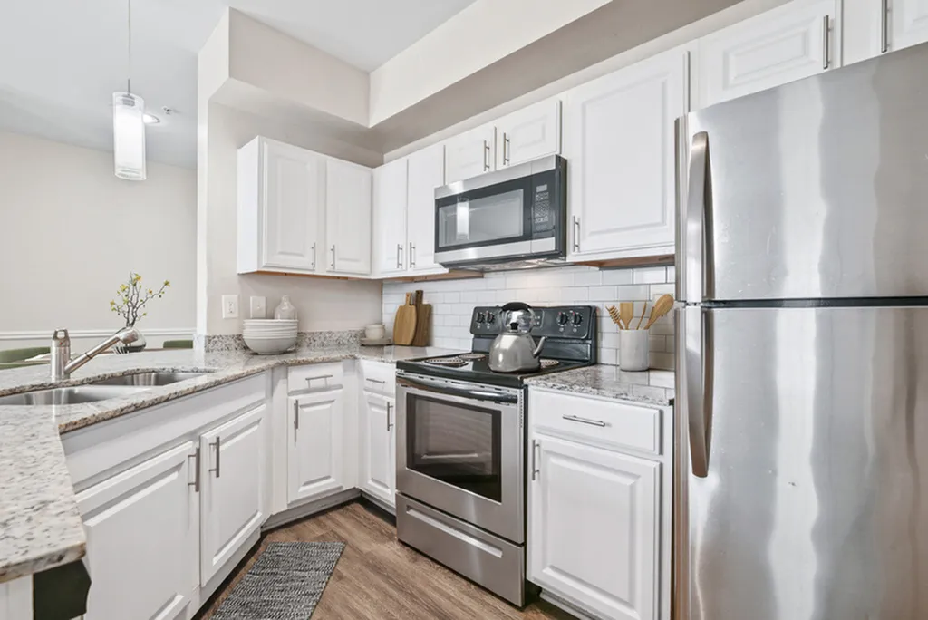 Kitchen with pendant lighting, granite counters, stainless steel appliances, white tile backsplash, hardwood flooring, and white cabinetry