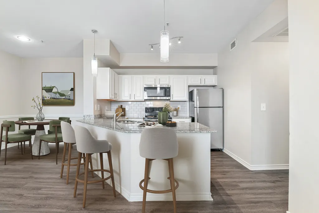 Kitchen with pendant lighting, granite counters, stainless steel appliances, white tile backsplash, hardwood flooring, bar chairs, dining table with chairs, and white cabinetry