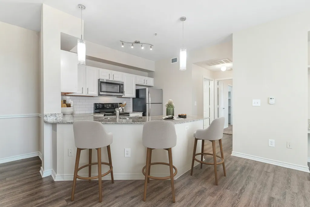 Kitchen with pendant lighting, granite counters, stainless steel appliances, white tile backsplash, hardwood flooring, three creme bar stools, nd white cabinetry