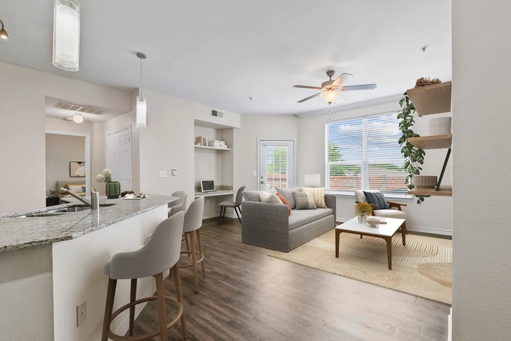 Living room with ceiling fan, wooden floors with a yellow rug, coffee table, grey couch, beige chair, with built-in shelving and desk area