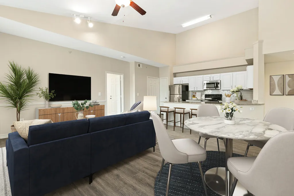 Open-concept living space with round dining table and white chairs, hardwood style flooring with blue rug, ceiling fan, blue couch, and wall mounted TV