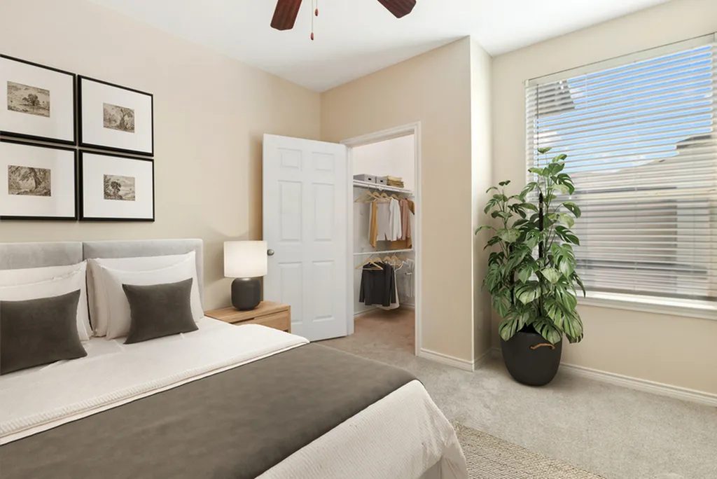 Bedroom with large bed with brown and white bedding, wall art, ceiling fan, open closet door, and large potted plant, with large windows