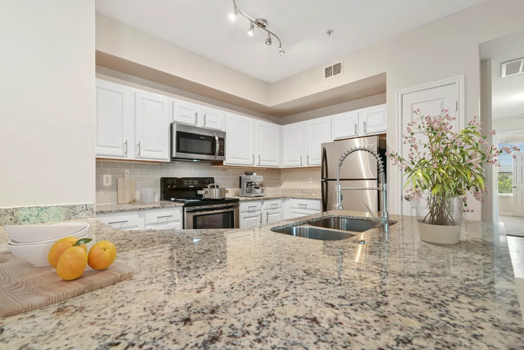 Kitchen with granite counters with potted plant and oranges,, white cabinetry hard wood flooring, and gooseneck faucet
