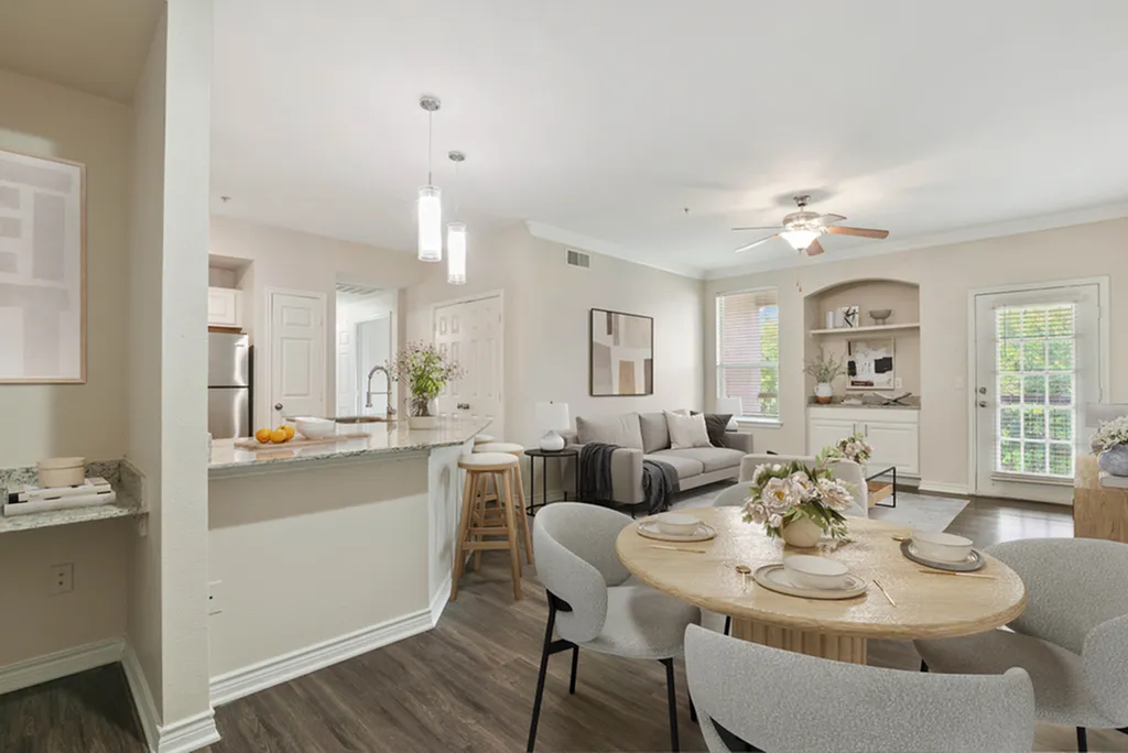 Open-concept dining area with round wooden table, kitchen bar with granite counters, pendant lighting, living room with ceiling fan, grey couch, and hard wood flooring