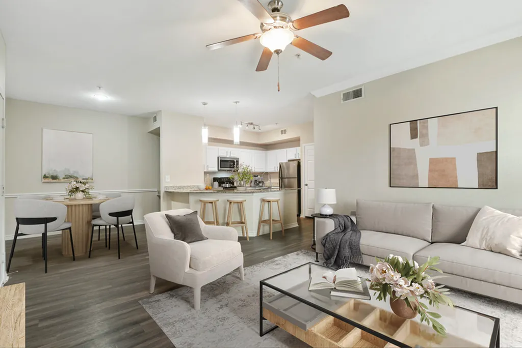 Open-concept living room with ceiling fan, hardwood flooring, grey rug, glass coffee table, cream chair, and wall art