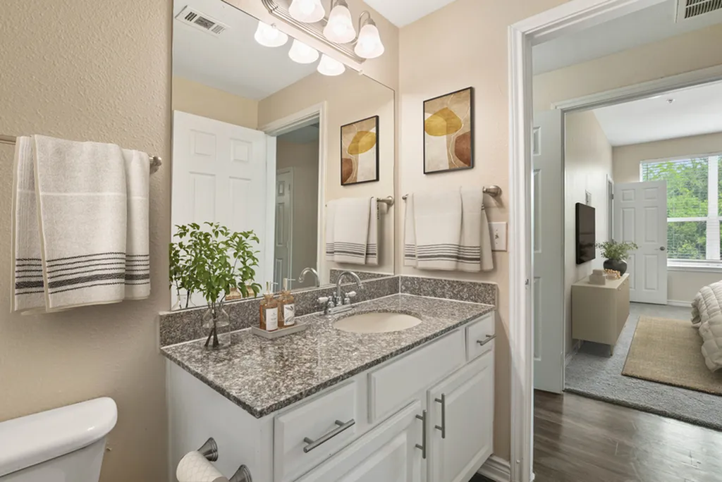 Bathroom with granite counter top, vanity lighting, toilet, bath tub, with door open showcasing bedroom