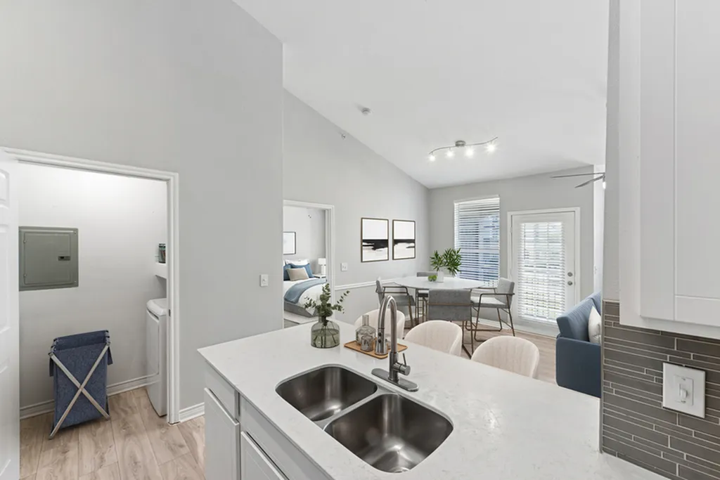 Open-concept kitchen with white quartz counters, gooseneck faucet undermount sink, laundry unit, creme bar chairs, over looking dining area