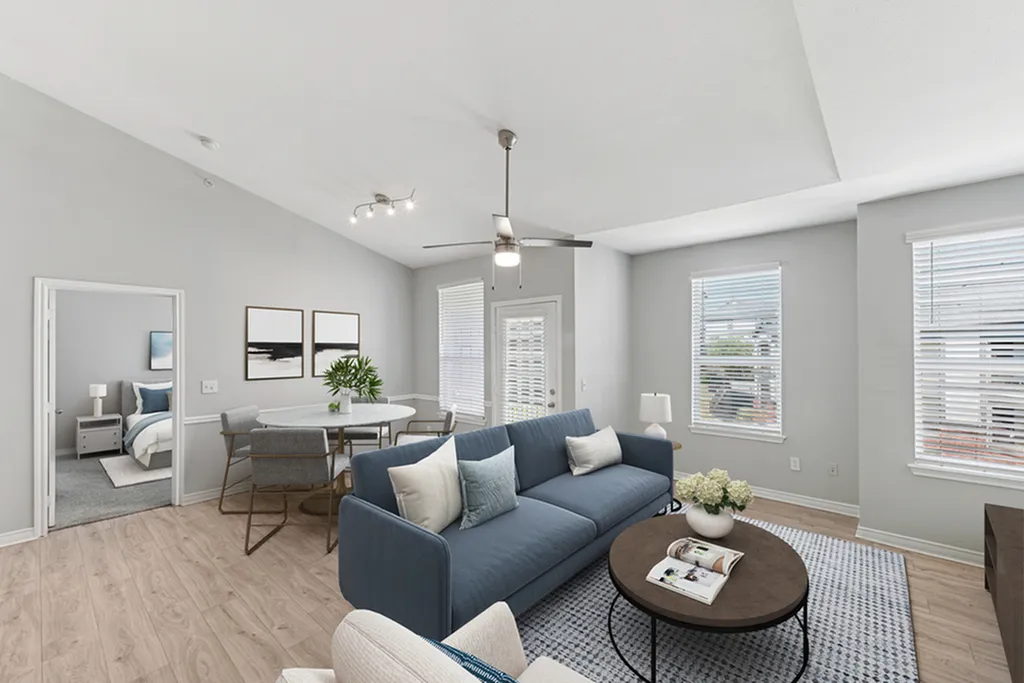 Open concept living room with ceinig fan, hard wood flooring, blue couch, round coffee table, dining area with table and chairs