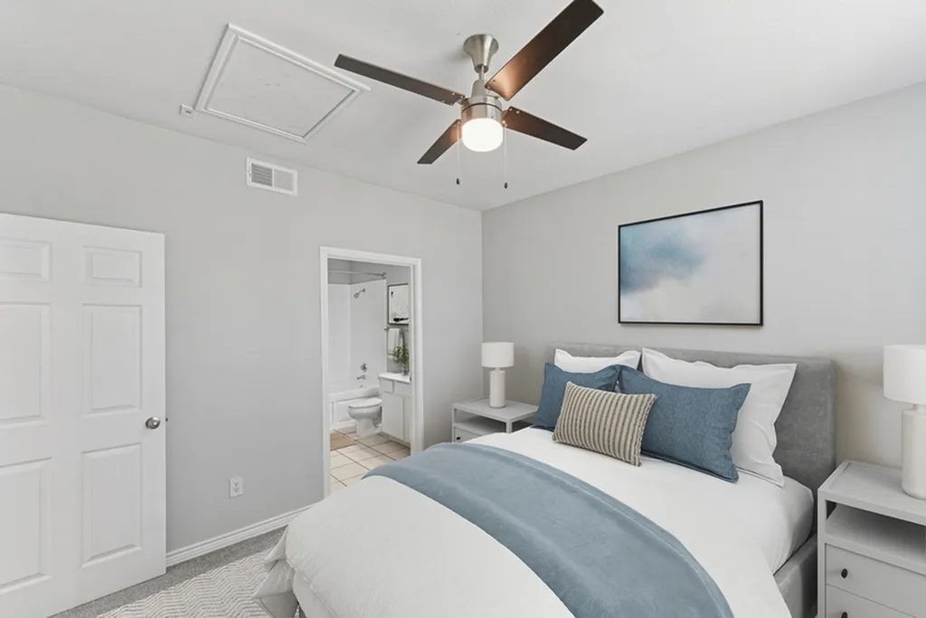 Primary bedroom with ceiling fan, large bed with blue and white bedding, grey night stand with lamp, and wall art